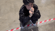 a man in a black jacket is kneeling down with his hands folded in front of his face