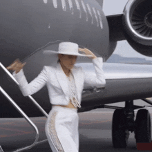 a woman in a white suit and hat is standing in front of a plane