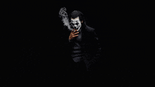 a man dressed as the joker is smoking a cigarette in a dark room .