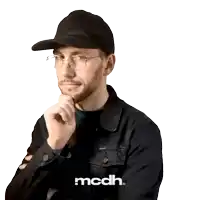 a man wearing glasses and a hat is standing in front of a white background that says mcdh