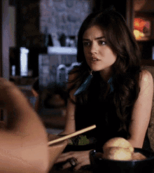 a woman is sitting at a table with a bowl of food and chopsticks