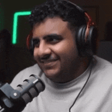 a man wearing headphones is talking into a microphone and smiling .