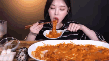 a woman is eating a plate of food with chopsticks and a spoon