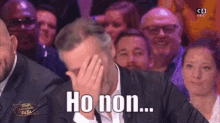 a man in a suit is covering his face in front of a crowd with the words ho non written on the screen .