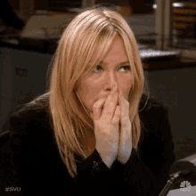 a woman with blonde hair is covering her mouth with her hands