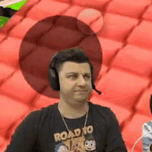 a man wearing headphones and a road to t-shirt is sitting in front of a red cushion .