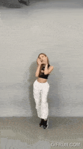 a woman in a black crop top and white pants is dancing with gifrun.com in the corner