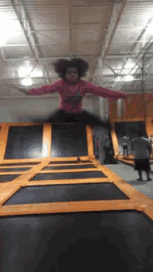 a girl in a pink shirt is jumping on a trampoline with her arms outstretched