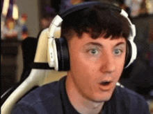a man wearing headphones is making a surprised face while sitting in a gaming chair .