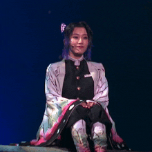 a woman with purple hair is sitting on a stage with a blue background