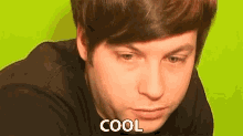 a young man in a black shirt is making a funny face and the word cool is on the bottom of his face .