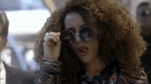 a woman with curly hair is wearing round sunglasses and making a face .