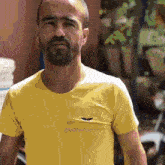 a man with a beard is wearing a yellow t-shirt with a logo on the front