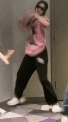 a woman in a pink shirt and black pants is dancing on a tiled floor .
