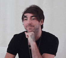 a man with a tattoo on his arm is wearing a black shirt and smiling .