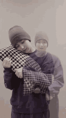 a man wearing a beanie and a purple sweater is holding a pillow .