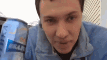 a man in a blue jacket is drinking from a can of soda .