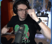 a man wearing glasses and headphones stands in front of a microphone with his fist raised