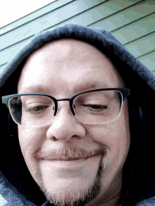 a man with glasses and a beard is wearing a hooded jacket