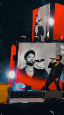a man singing into a microphone on a stage with a large screen behind him
