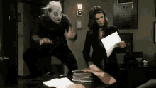 a man wearing a mask is standing next to a woman holding a piece of paper in an office .