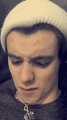 a young man wearing a white beanie and a necklace with a key pendant