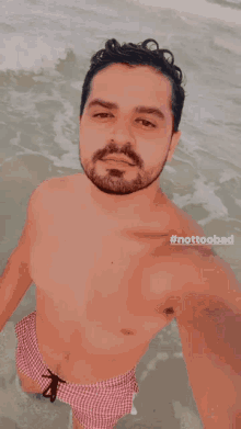 a shirtless man taking a selfie in the ocean with #nottoobad written below him