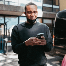 a man wearing a black face mask is looking at his phone