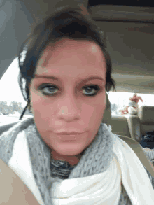 a woman in a car with a scarf around her neck looks at the camera