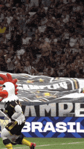 a rooster mascot is running on a soccer field in front of a brasil banner