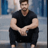 a man with a beard wearing a black shirt is sitting down