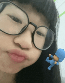a girl wearing glasses has a small blue toy in her hand