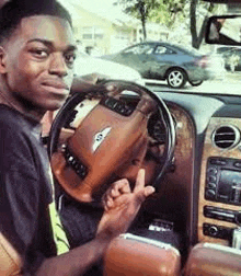 a young man is sitting in the driver 's seat of a car and holding the steering wheel .
