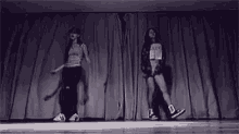 a couple of women are dancing on a stage in front of a curtain .