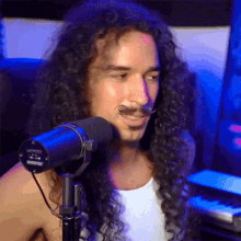 a man with long curly hair and a mustache is sitting in front of a shure microphone