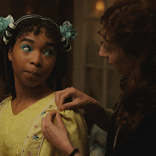a woman is adjusting a yellow dress on a young girl