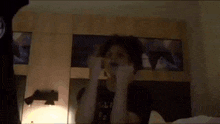 a young boy is sitting on a bed in a dark room with his hands in the air .