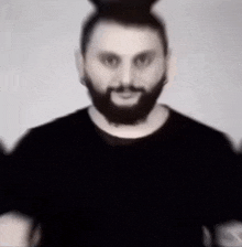 a man with a beard is wearing a black t-shirt and a black hat .