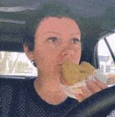 a woman is driving a car and eating a donut