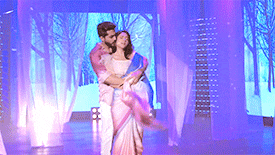 a man is holding a woman in his arms on a stage in front of a screen .