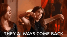 two women are sitting next to each other in a room and pointing at something .