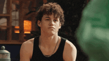 a young man with curly hair wearing a black tank top and a chain around his neck