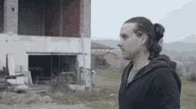 a man with long hair and a ponytail stands in front of a building