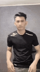 a young man in a black t-shirt is standing in front of a mirror and looking at the camera .