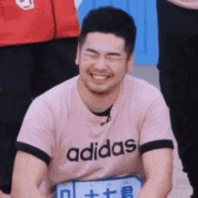 a man wearing a pink adidas t-shirt is laughing with his eyes closed .