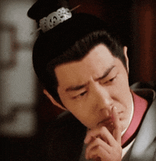 a man with a bun on his head has his finger on his nose