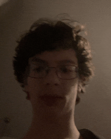 a young man wearing glasses looks at the camera in a dark room