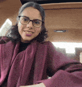 a woman wearing glasses and a purple coat is smiling