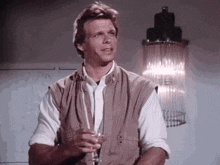 a man in a vest is holding a glass of wine in front of a lamp .