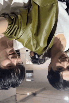 a man in a green leather jacket is laying down next to another man in a white shirt